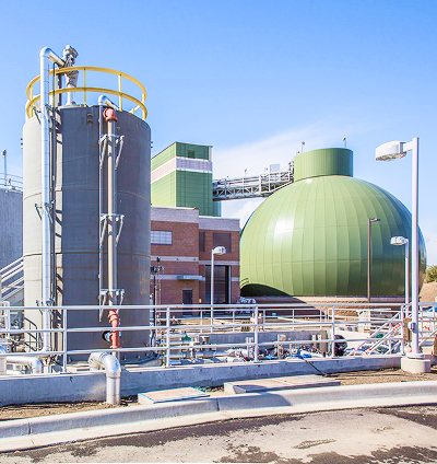 Industrial facility with a large green dome, tanks, and a network of pipes.