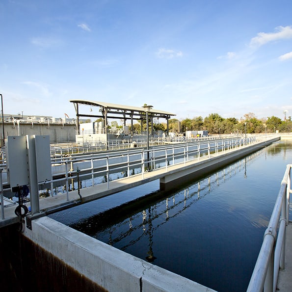 Water treatment facility with elevated walkways and a rectangular clarifier basin under a clear blue sky.