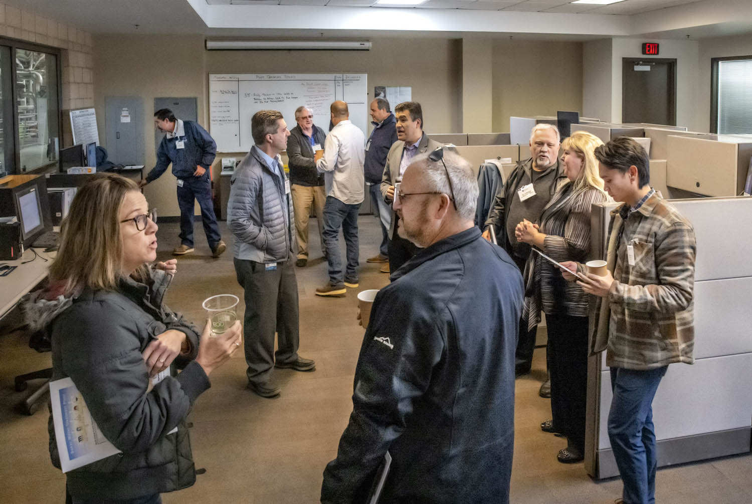 Group of professionals in a modern office talking and networking near cubicles.
