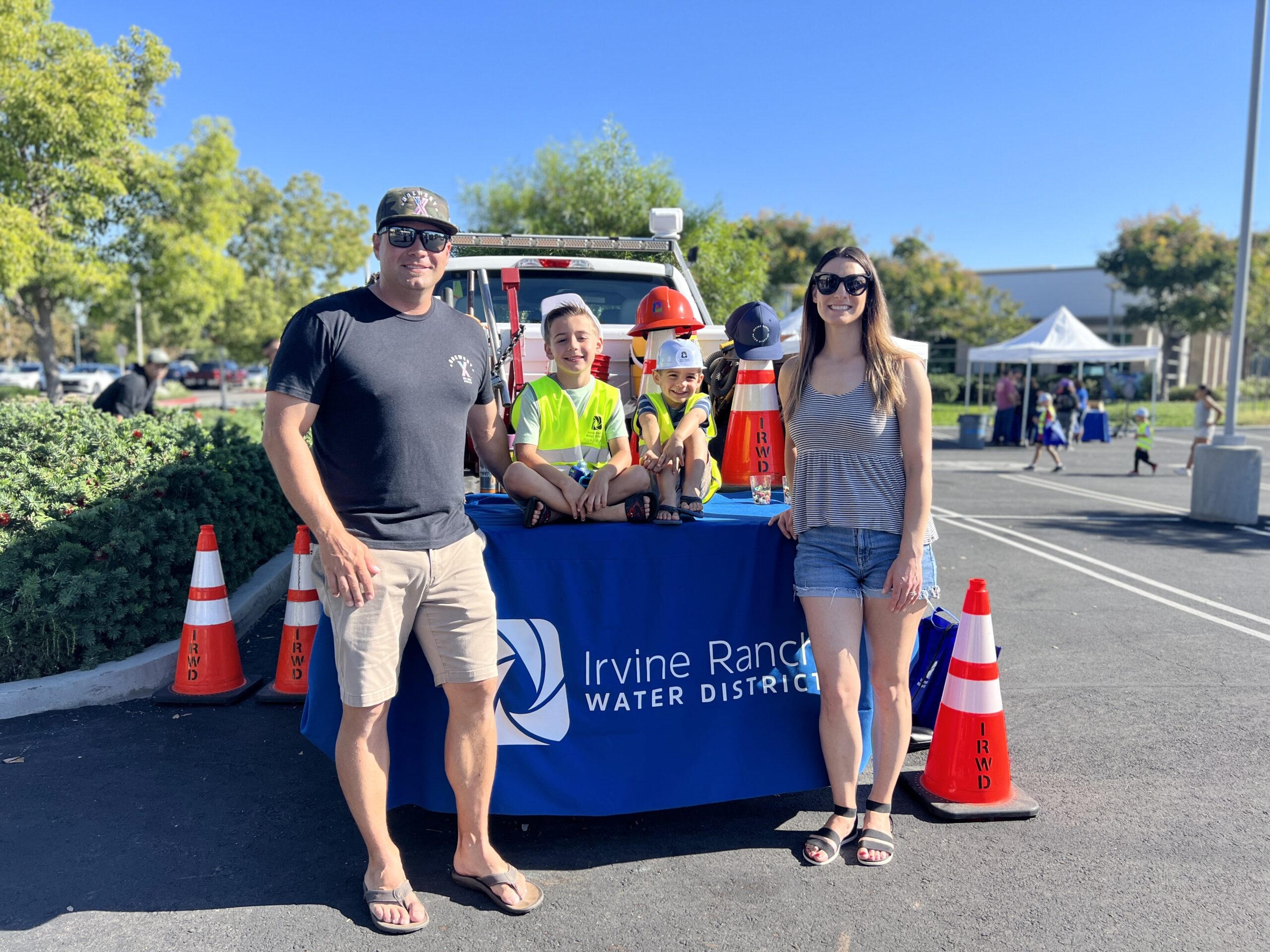 Family posing at Irvine Ranch Water District booth with kids in safety vests and a service truck in the background.