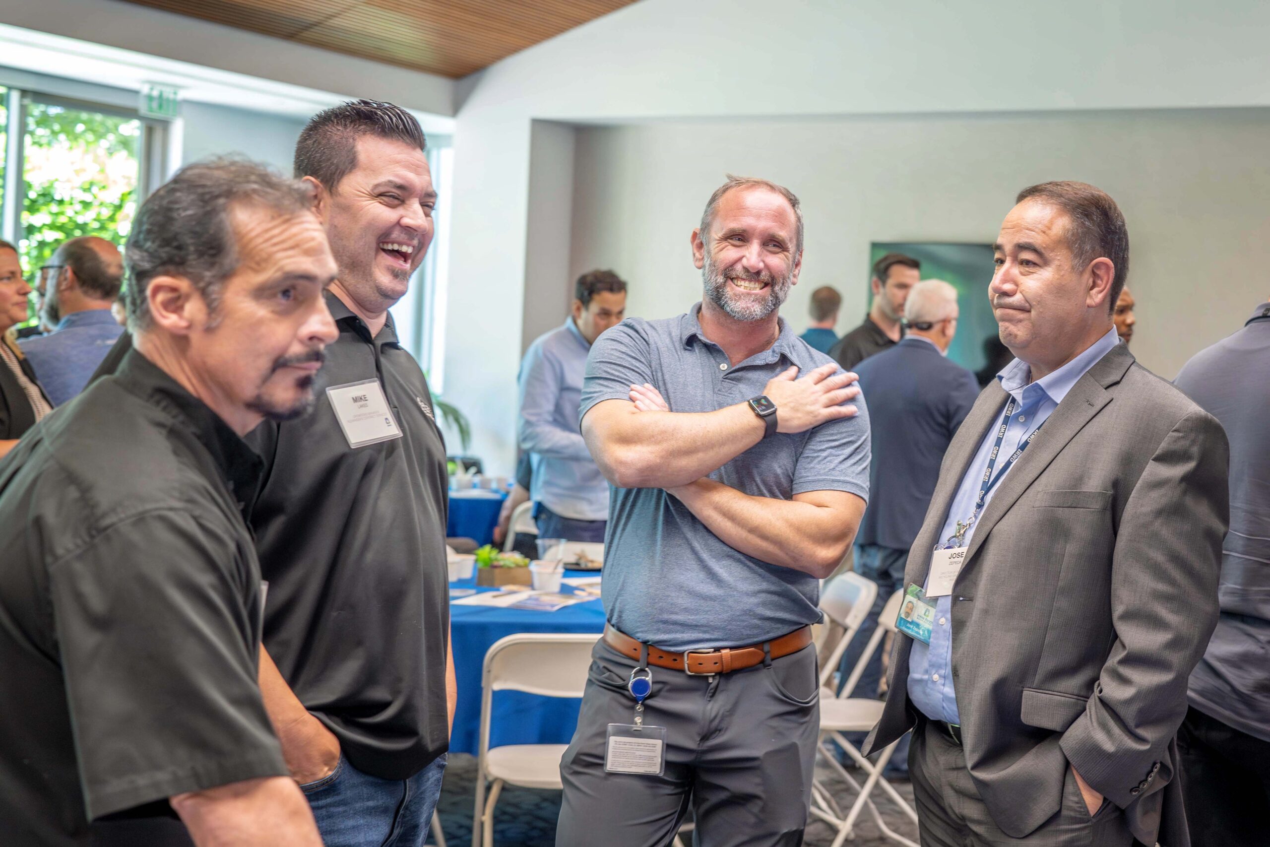 Group of men networking at a conference, smiling and talking in a bright room.