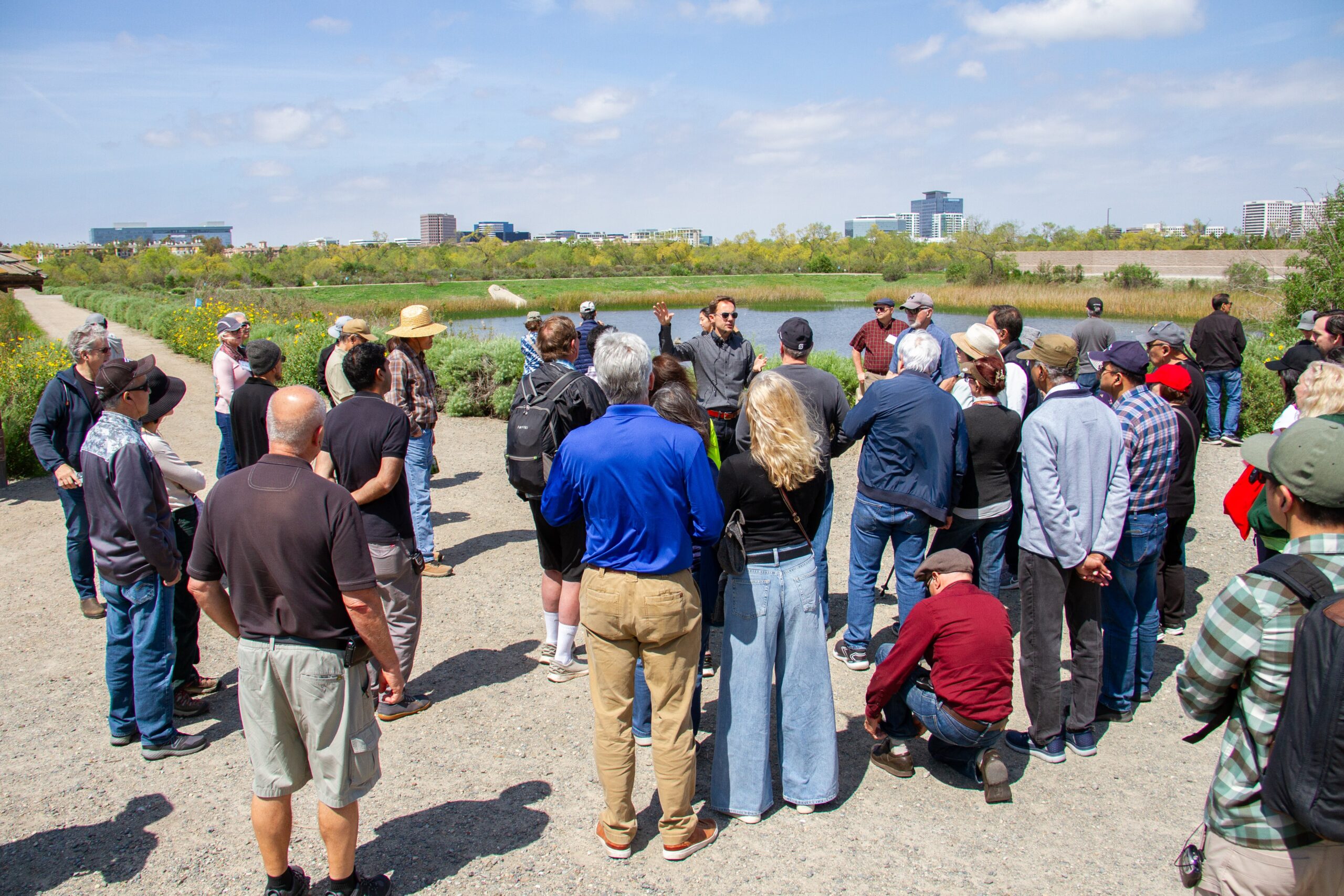 Group of people on a guided outdoor tour by a wetlands area with a speaker addressing the crowd