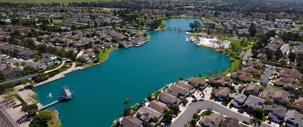Aerial view of a suburban lake community with waterfront homes, a turquoise lake, docks, and a small bridge.