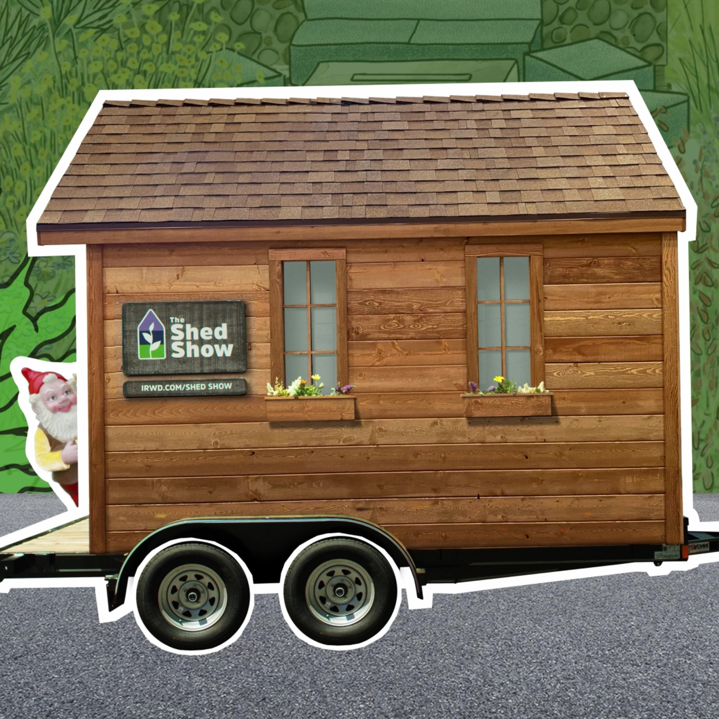 Wooden shed mounted on a wheeled trailer with two narrow windows and flower boxes beneath them, featuring a 'The Shed Show' sign.