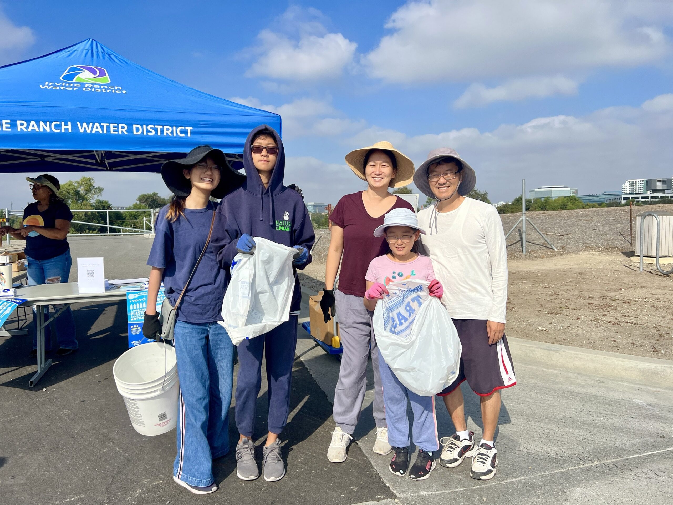 Group of volunteers at Irvine Ranch Water District cleanup under a blue canopy, posing with trash bags.