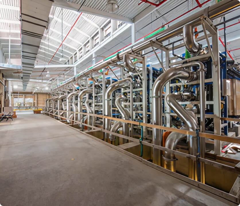 Industrial plant with a network of large stainless steel piping and machinery along a walkway