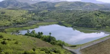 Scenic hillside landscape with a calm lake, green valleys, and distant mountains.