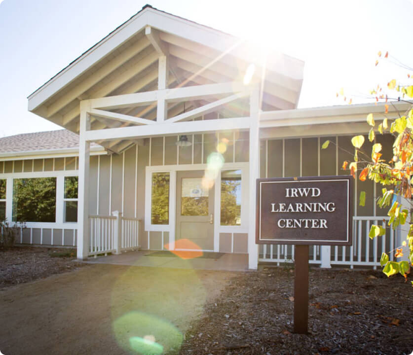 Front entrance of the IRWD Learning Center with gray siding, a white-framed porch, and sun glare