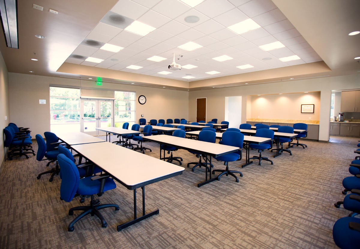 Bright training room with rows of blue swivel chairs and long beige tables