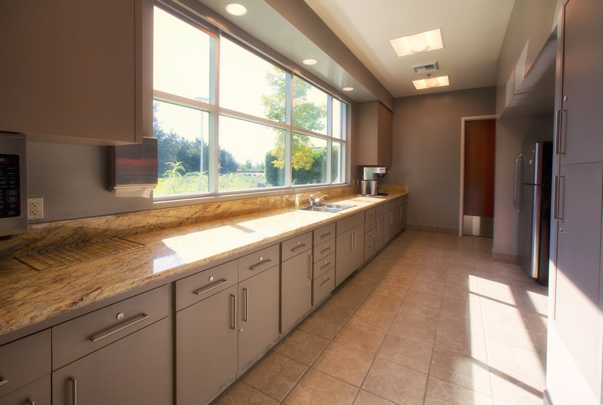 Modern kitchen with grey cabinets, a long granite counter, and a large window overlooking greenery