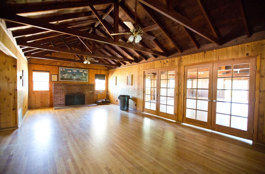 Wood-paneled living room with an exposed beam ceiling, brick fireplace, and French doors.