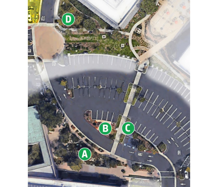 Aerial view of a large curved parking lot with green lettered markers A–D identifying key areas, surrounded by buildings and walkways.