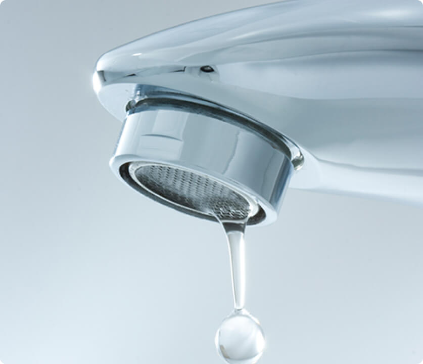 Close-up of a chrome faucet dripping a single clear water droplet