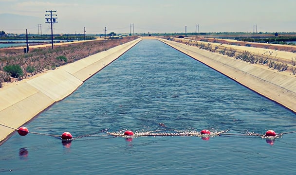 Long concrete irrigation canal with red buoys strung across the water and power lines in the distance.