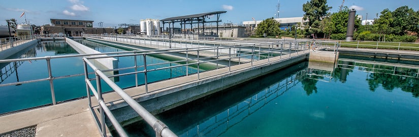 Wastewater treatment plant with rectangular basins and metal walkways under a sunny sky
