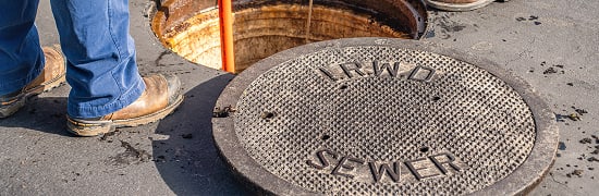 Construction worker standing near a circular street manhole cover labeled SEWER.
