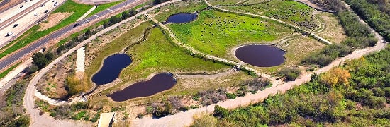 Aerial view of a park with several irregular ponds and winding paths beside a highway.