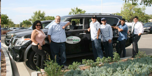 Group of diverse adults posing beside a black RideShare van in a parking lot.