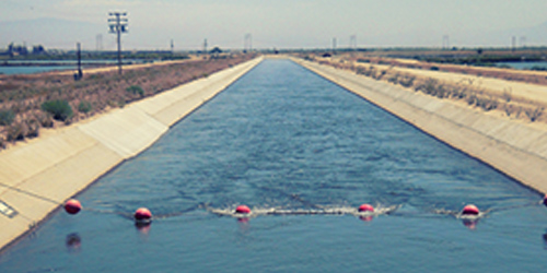 Irrigation canal with red buoys across a concrete-lined channel and dry fields on both sides.
