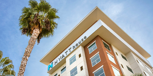 Hyatt House hotel building with a tall palm tree and clear blue sky.