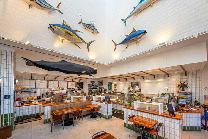 Restaurant interior with white tile walls, counters, and oversized mounted fish displays on walls and ceiling.