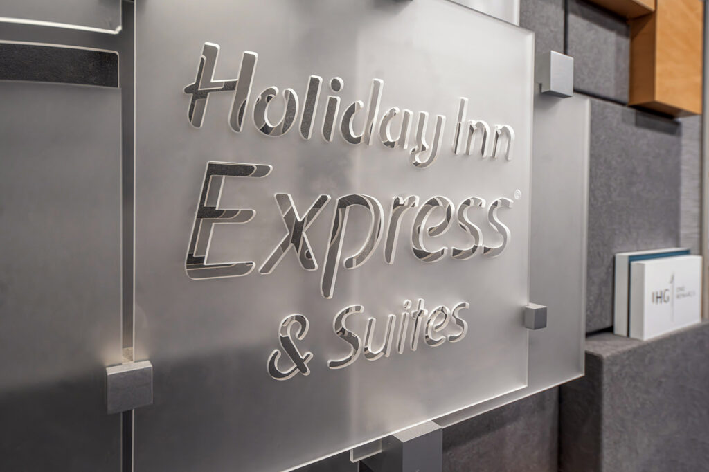 Brushed metal sign reading 'Holiday Inn Express & Suites' mounted on a textured wall.