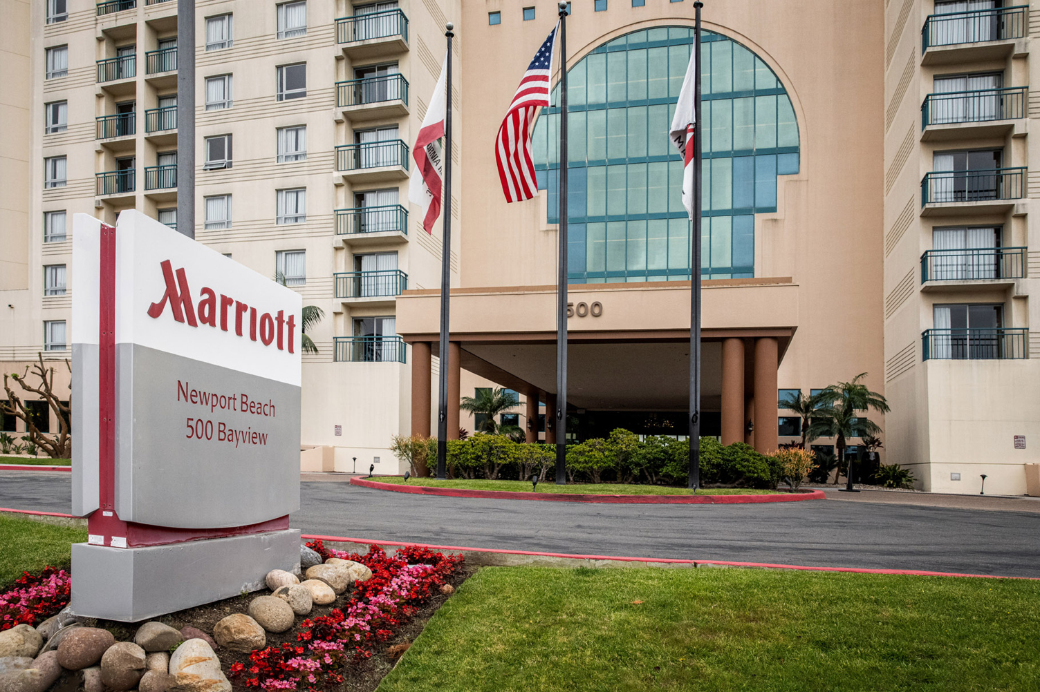 Marriott Newport Beach hotel entrance with flagpoles, curved glass atrium and beige exterior