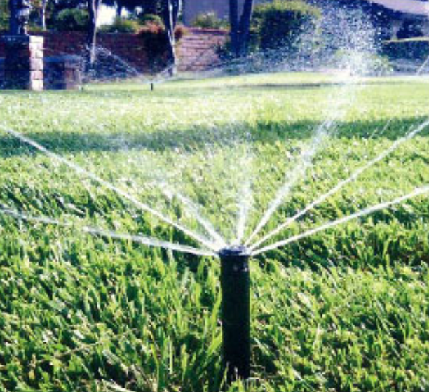 Automatic lawn sprinkler spraying water across a green, well-maintained lawn.