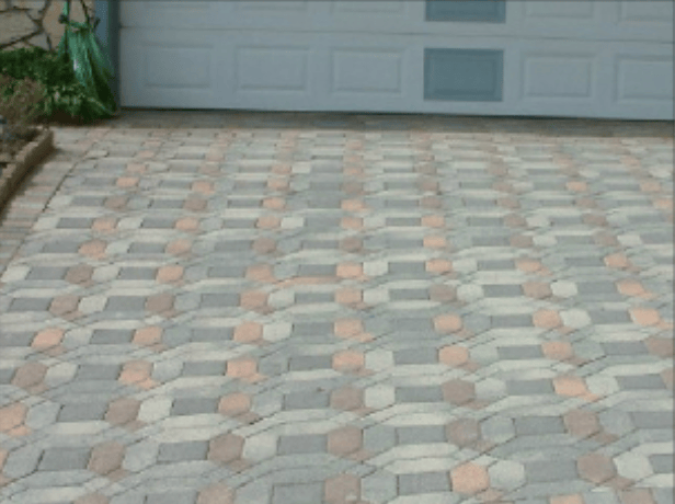 Driveway of interlocking hexagonal pavers in gray and reddish tones leading to a light gray garage door.