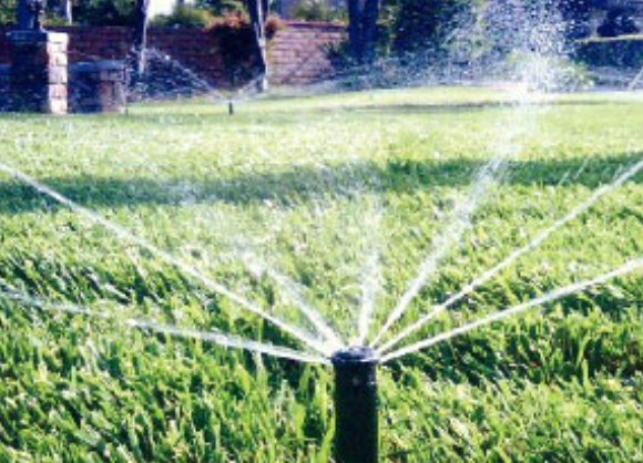 Lawn sprinkler sprays water across green grass in a sunny garden.