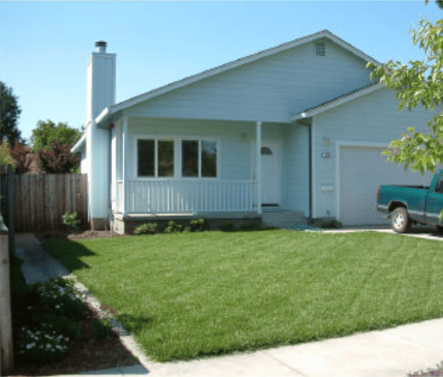 Light-blue ranch-style house with a small covered front porch, white railing, and a well-kept green lawn.