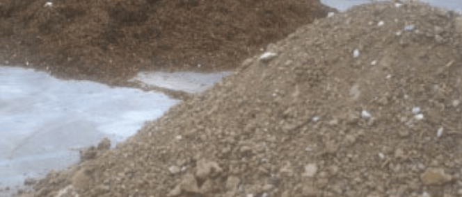 Two mounds of gravel and dirt with a wet concrete surface on the left