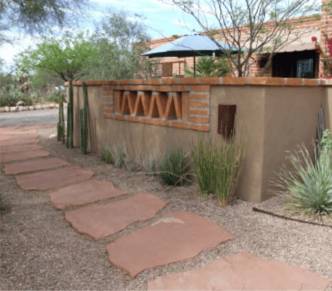 Desert backyard with a stepping-stone path, adobe wall, and a shaded patio area.