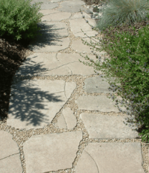 Stone pathway with irregular flagstone pavers and gravel joints, flanked by green shrubs.