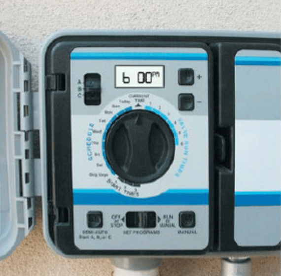 Outdoor irrigation timer with a rotary dial and digital display mounted on a wall.