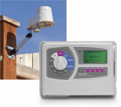 Home security camera mounted on a wooden fence beside a digital irrigation timer.