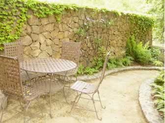 Outdoor patio with a metal table and chairs beside a stone wall covered in ivy.
