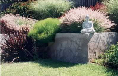 Buddha statue seated on a stone pedestal amid ornamental grasses and a neatly trimmed lawn