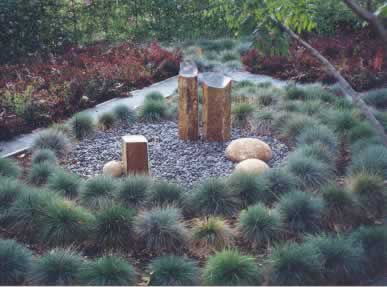 Circular garden bed featuring three vertical stone sculptures framed by blue fescue grass.