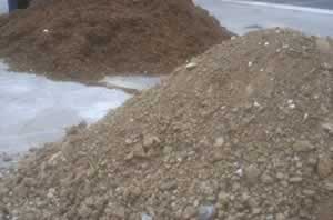 Two large piles of gravel and soil beside a paved area at a construction site.