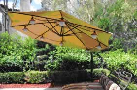 Yellow patio umbrella over a curved wooden bench in a sunny garden with green hedges.