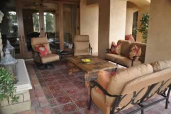 Covered outdoor patio with beige cushioned wicker seating around a wooden coffee table.