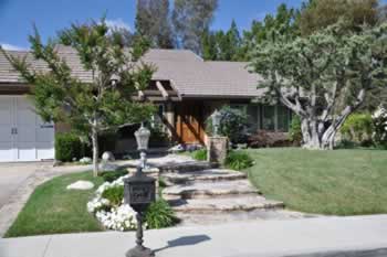 Front view of a suburban single-family home with stone steps, a mailbox, and a well-kept front lawn.